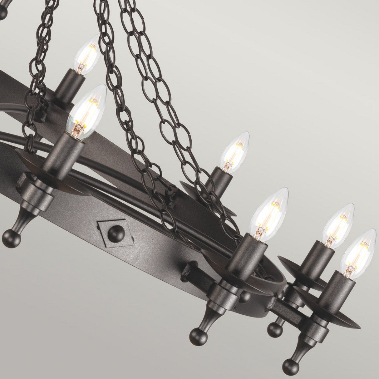 This rustic chandelier, echoing medieval craftsmanship with its industrial influence, boasts an iron ring in a Graphite Black finish, supported by multiple chains. It accommodates eight candle-shaped light bulbs, evenly distributed around the circular frame, producing a warm and inviting glow similar to that of the Warwick 12 Light Chandelier - Graphite Black.