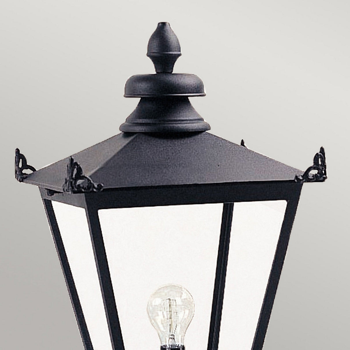 A close-up of the Wilmslow 1 Light Outdoor (Head Only) in black showcases its Victorian design with a pointed top and clear glass panels. Inside, a single bulb illuminates against a light gray background.