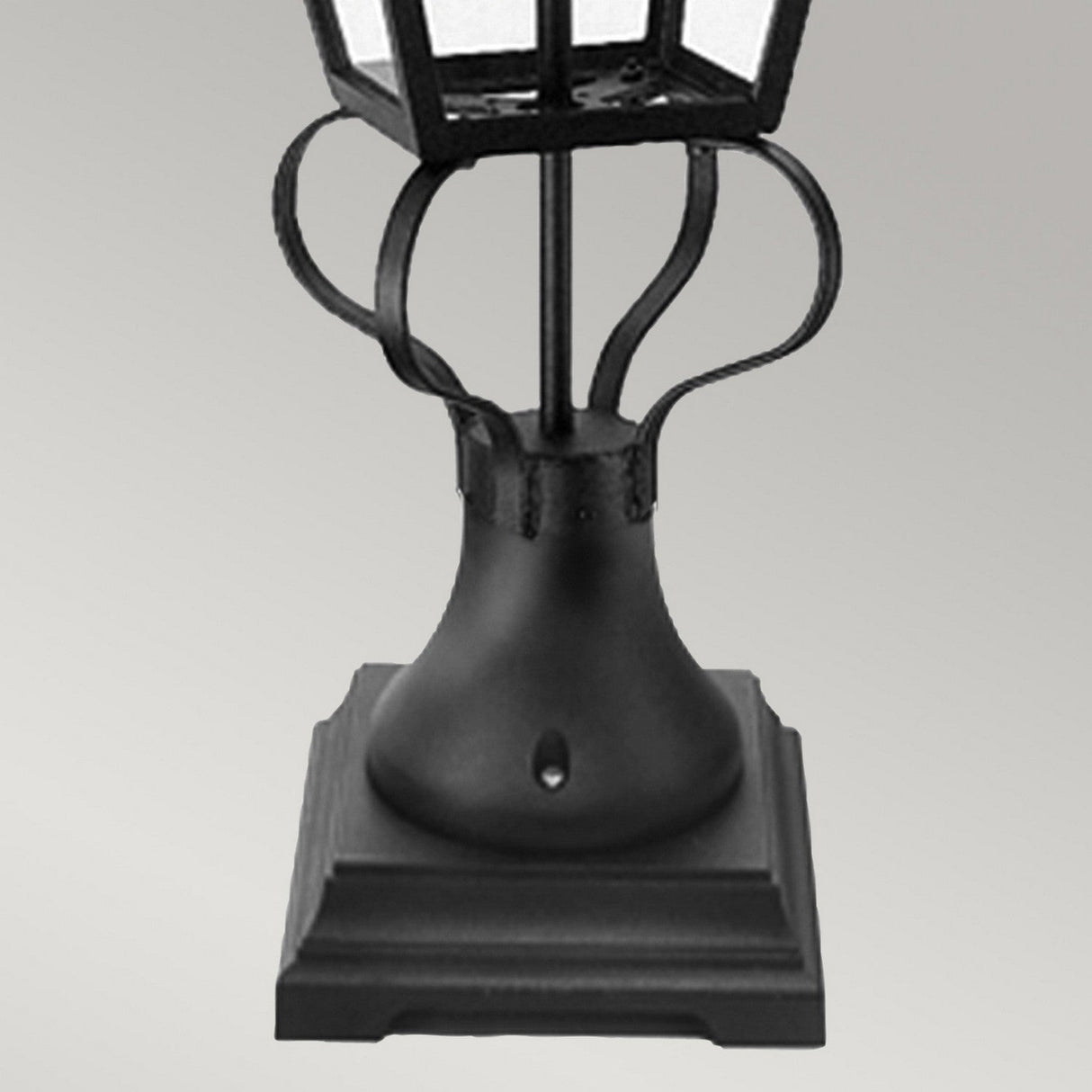 The Wilmslow 1 Light Pedestal Light in black, featuring ornate Victorian-style metalwork and a square pedestal, stands as a striking piece of outdoor lighting against a plain gray background.