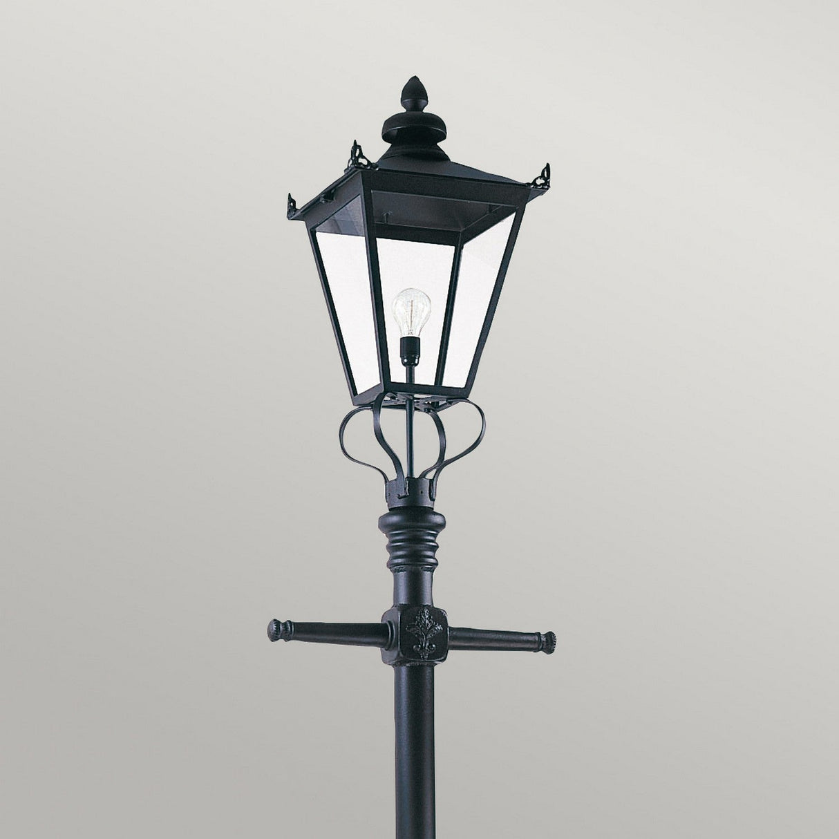 The Wilmslow 1 Light Lamp Post - Black features a durable cast aluminum construction with a clear glass lantern and visible light bulb, all set against a plain gray background to highlight its vintage, Victorian-inspired design in outdoor lighting.