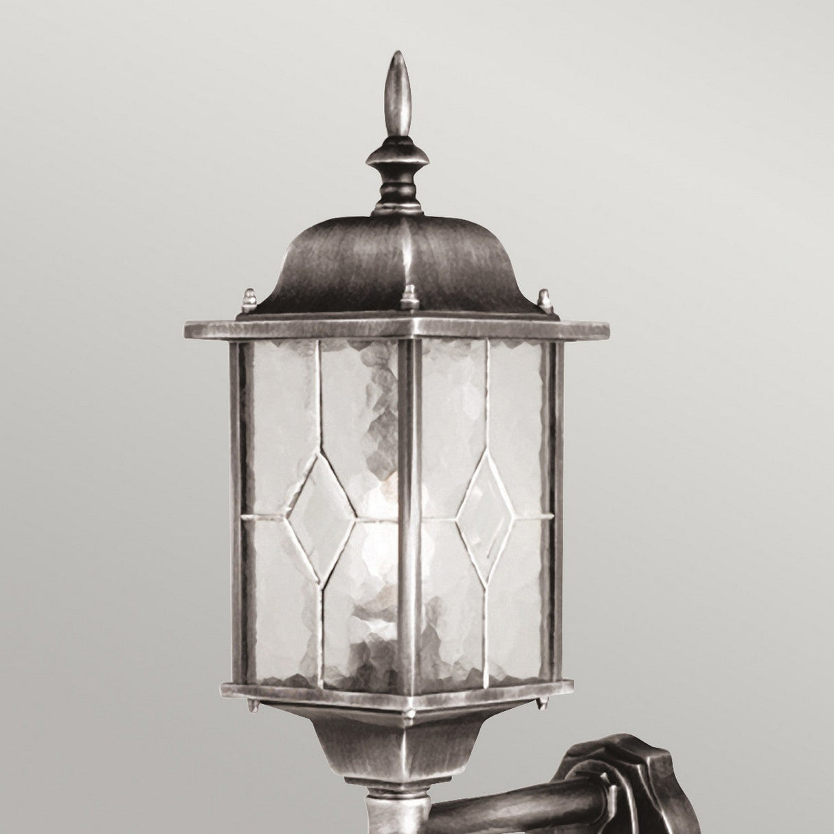 The Wexford 1 Light Outdoor Up Wall Light with PIR in Black/Silver is a vintage-style wall lantern featuring a decorative finial on top. It has a metal frame and hand-leaded glass panels with diamond patterns, mounted on a short arm against a plain background. An optional PIR sensor enhances its functionality.