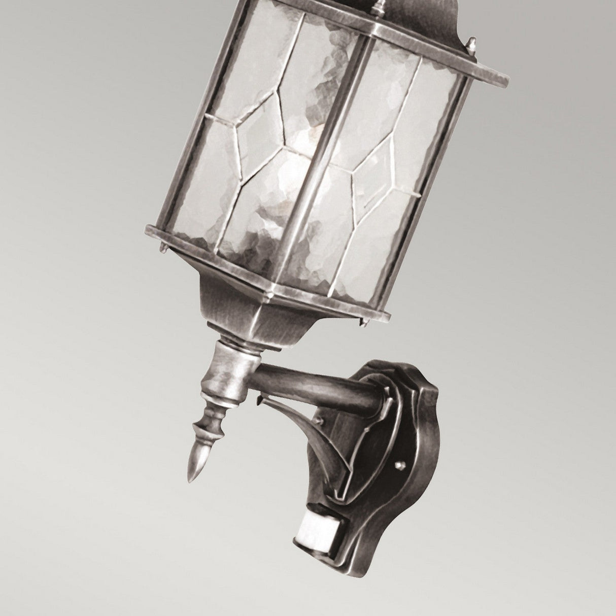 The Wexford 1 Light Outdoor Up Wall Light with PIR - Black/Silver is a vintage-style wall lantern featuring hand-leaded geometric glass, elegantly mounted on a decorative metal bracket. Its charm is perfectly complemented by the discreet PIR sensor at the base against a neutral gray background.