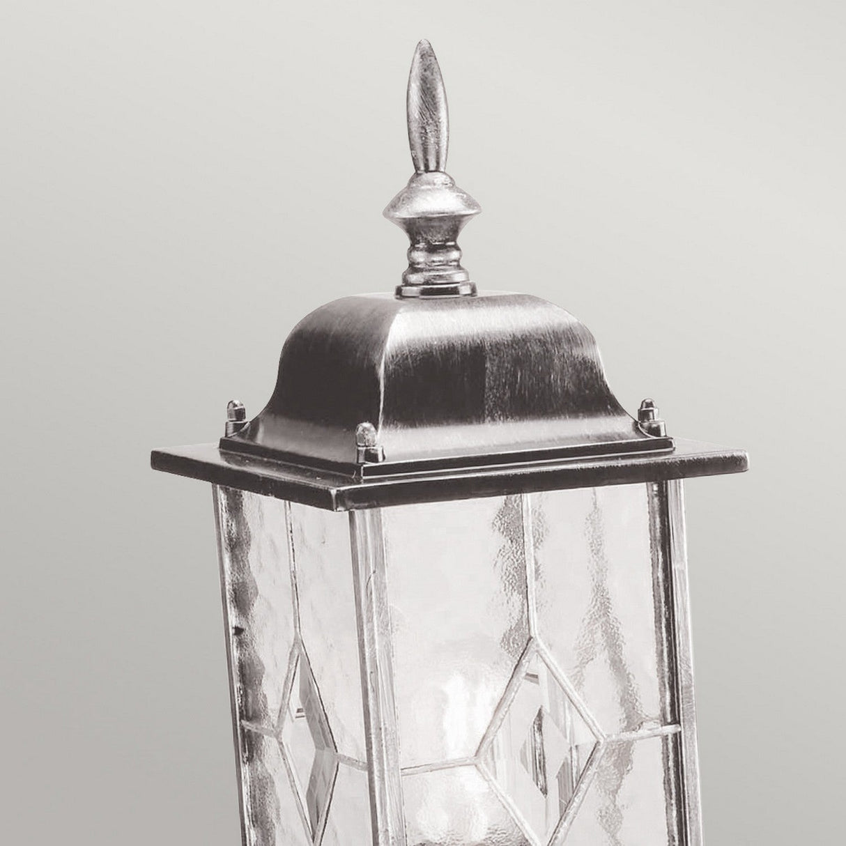 A Wexford 1 Light Pedestal Light in black and silver, featuring a vintage-style design with a pointed finial top and leaded lantern glass panels showcasing a diamond pattern, set against a plain gray background.