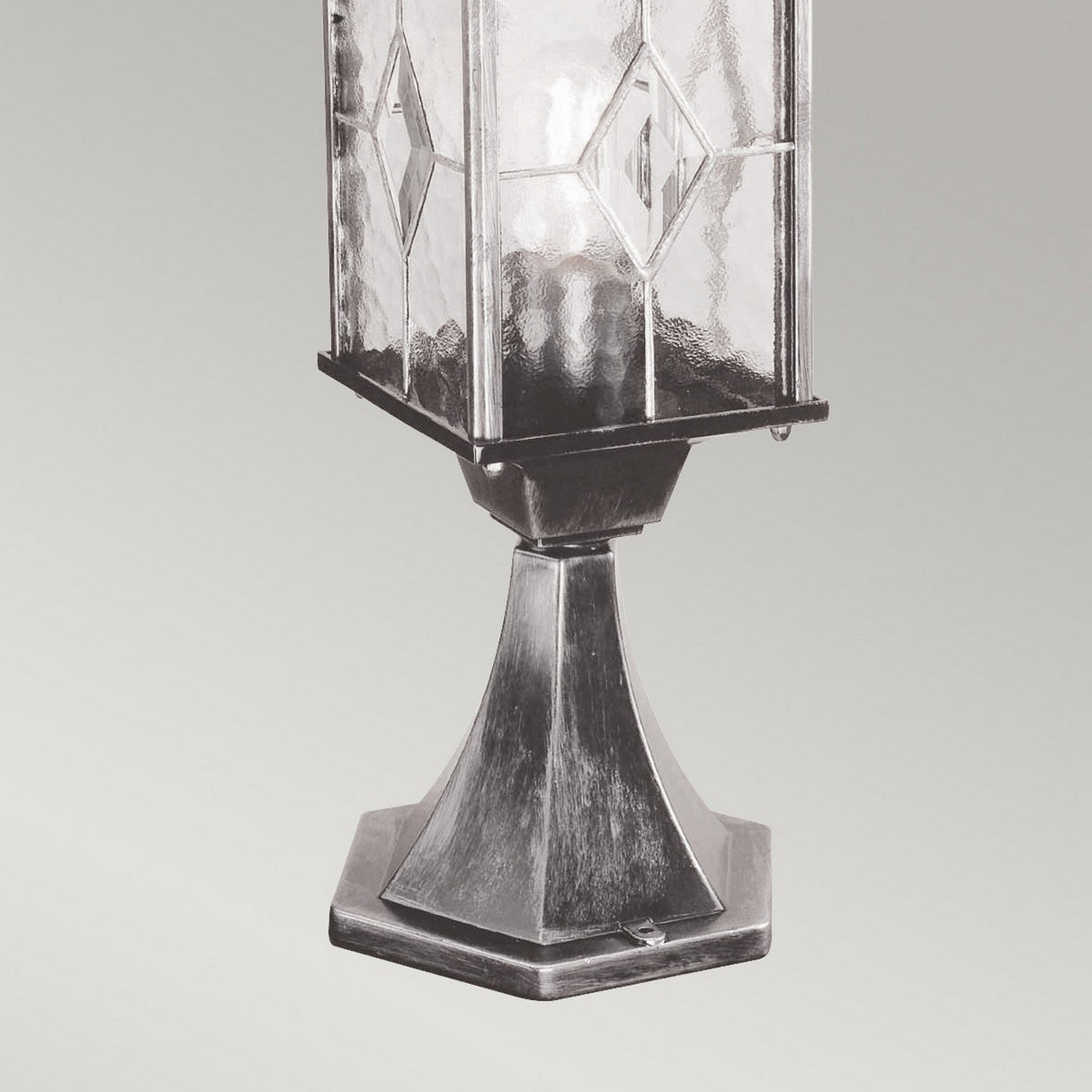 The Wexford 1 Light Pedestal Light - Black/Silver is a vintage-style lantern with geometric patterned glass and a hexagonal metal base, ideal for outdoor lighting, shown against a light gray background.