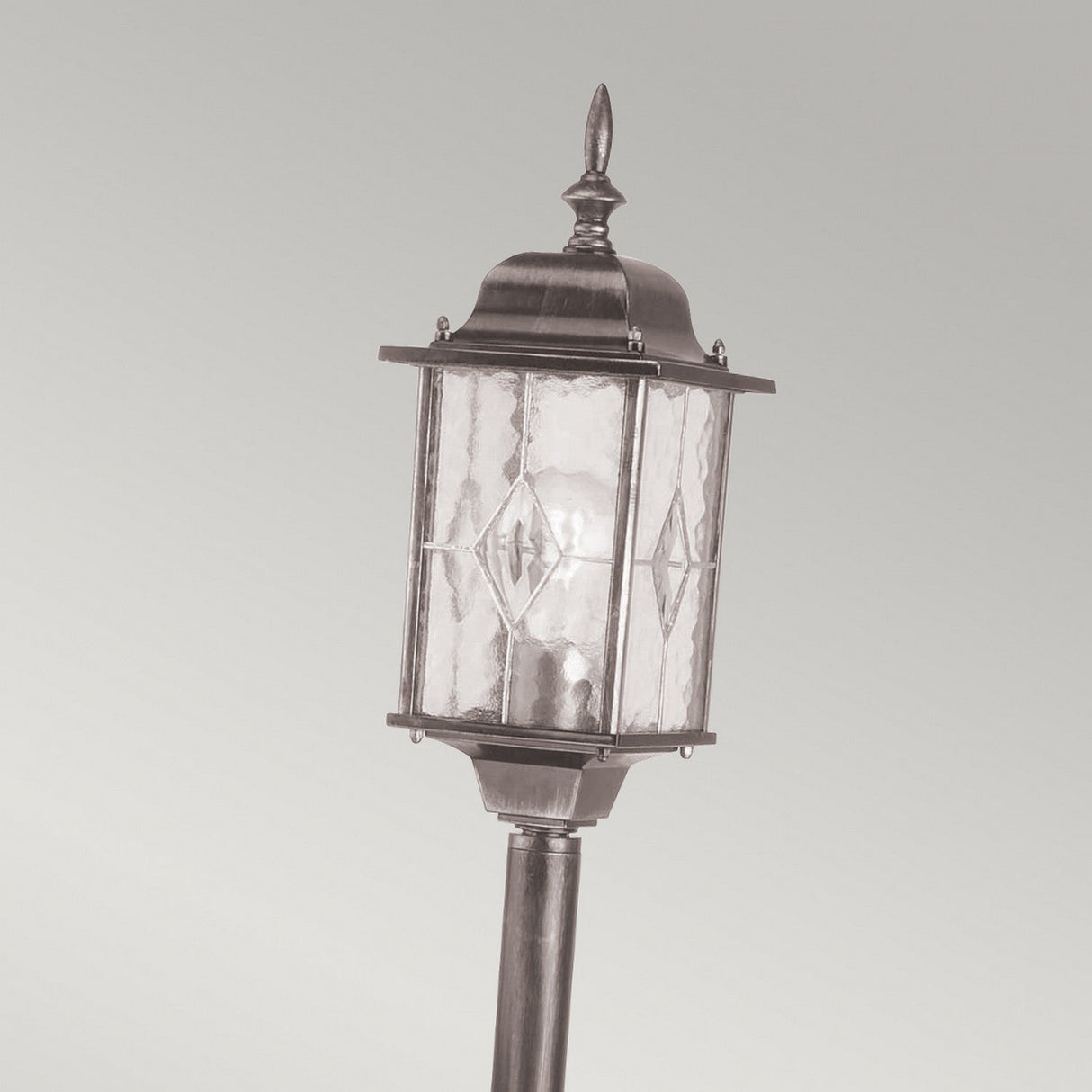 Introducing the Wexford 1 Light Pillar Light in Black/Silver: This vintage-style outdoor lamp is crafted from durable materials and showcases a clear glass lantern that encases a light bulb. It features decorative metal elements and a pointed top, embodying traditional design against a plain, light gray background.