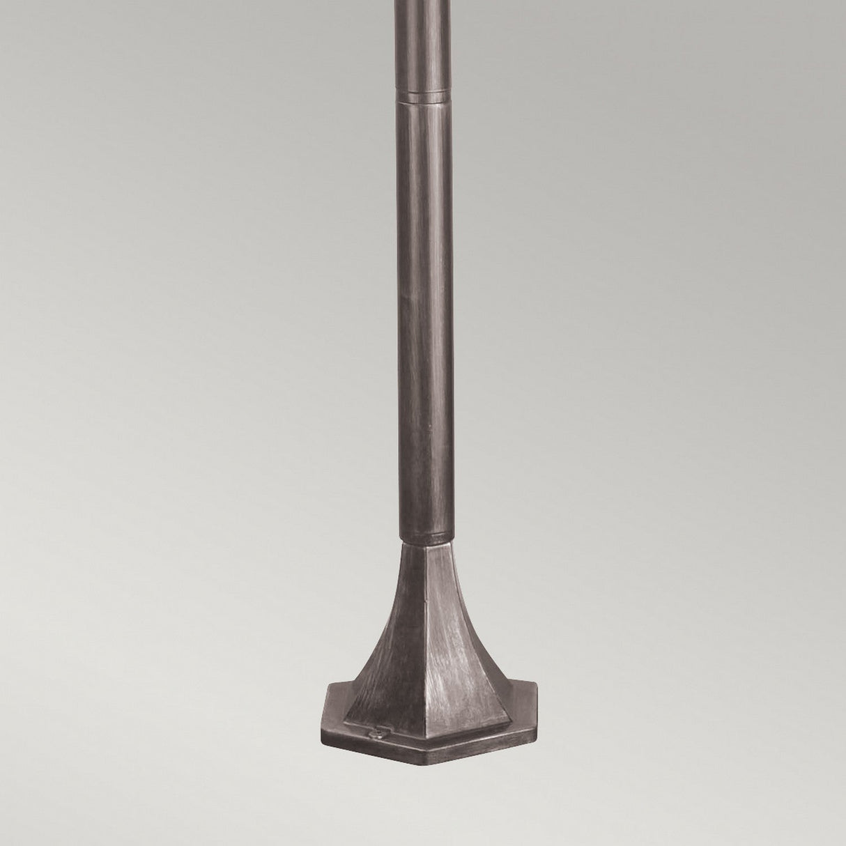 A close-up view of the Wexford 1 Light Pillar Light, showcasing its sleek, cylindrical pole and wide, angular square base crafted from durable materials. The lamp exudes traditional design elements and is set against a plain gray background.