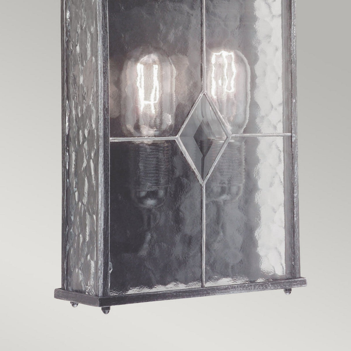 The Wexford 2 Light Outdoor Wall Light in Black/Silver epitomizes traditional elegance with its rectangular textured glass design, showcasing a central diamond-shaped hand-leaded glass accent. The fixture features two visible vintage-style light bulbs that illuminate behind the glass, while the metallic-finished frame enhances its charm.
