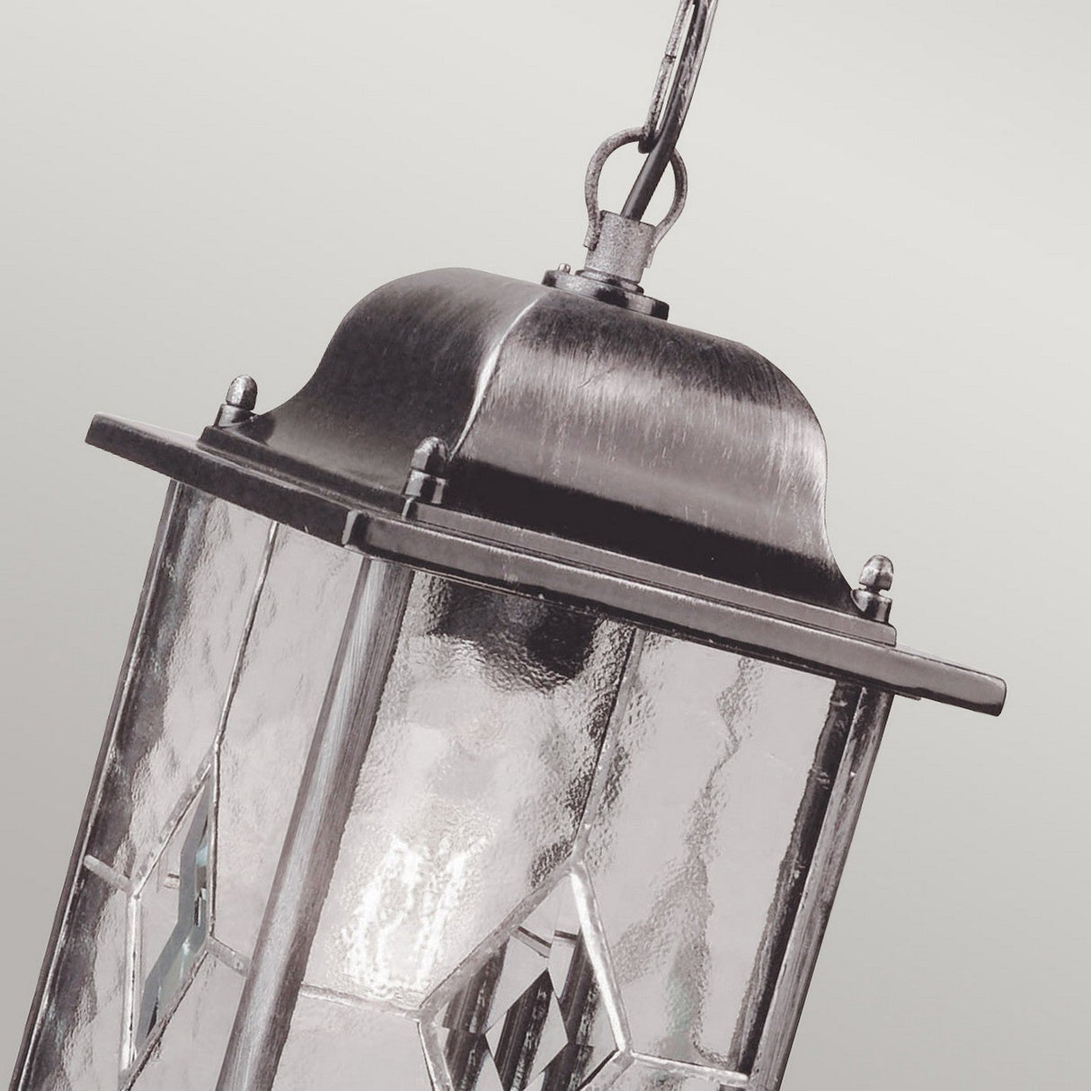 The Wexford 1 Light Outdoor Chain Pendant in Black/Silver showcases a vintage lantern design with a metal top and decorative glass panels. Its weather-resistant construction guarantees durability. Hung by a short chain, it contrasts elegantly against the subtle gray background.