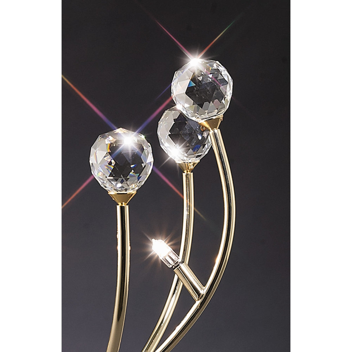 The Xeena 3 Light Crystal Table Lamp in French Gold features three gold stems holding crystal-like spheres that shimmer with light, creating a luxurious and elegant accent perfect for dark backgrounds.