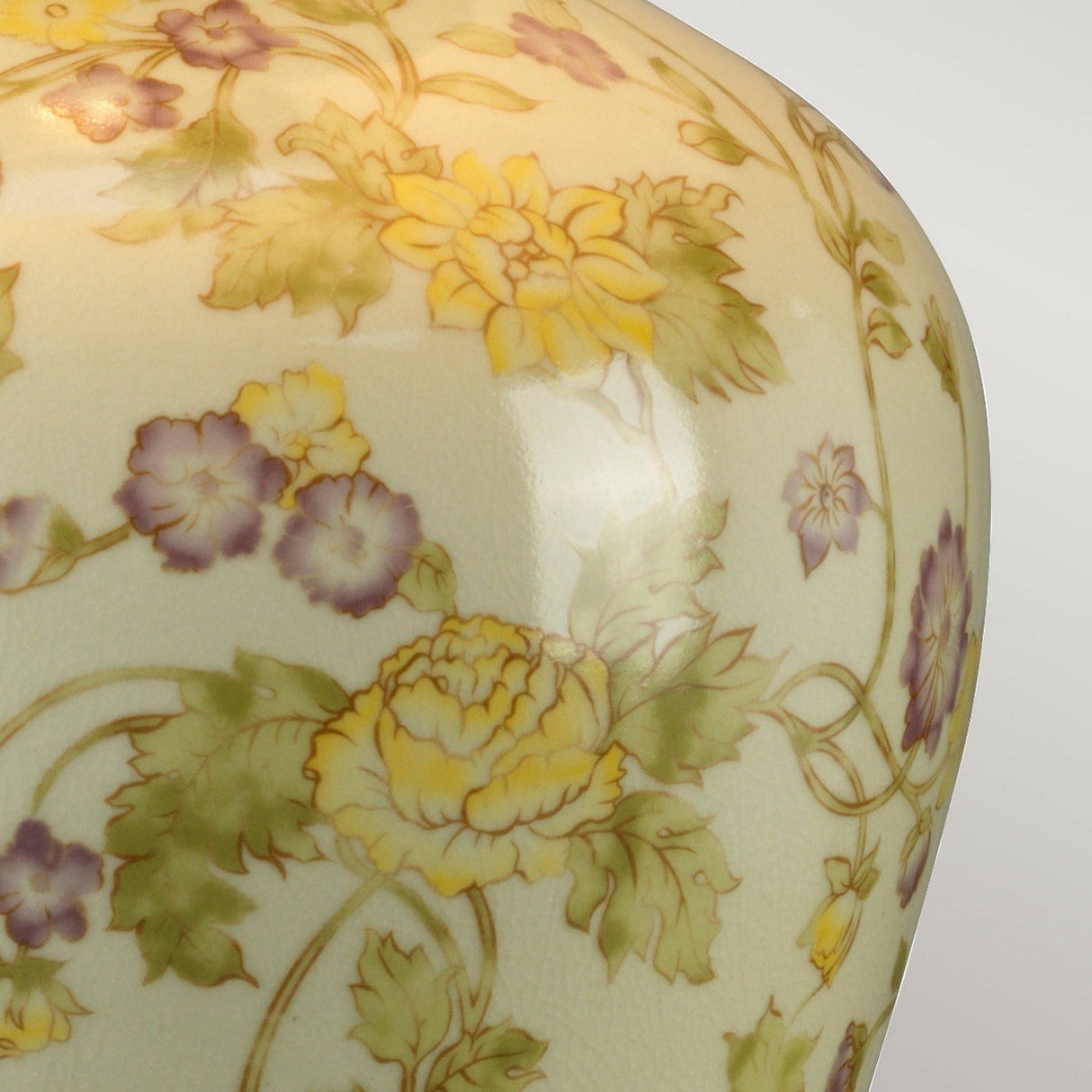 Here is a close-up of the Yellow Flowers 1 Light Table Lamp, featuring a decorative ceramic surface with a floral design. The pattern showcases yellow and purple flowers alongside green leaves on a light background, reminiscent of the elegance and intricacy of Chinese porcelain, complete with elegant swirls and a glossy finish.