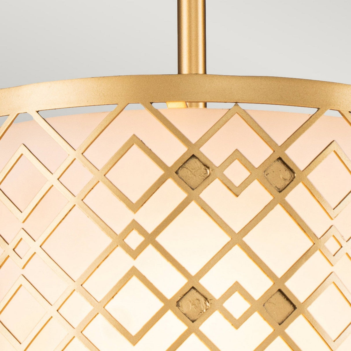 Close-up of the Ziggy 1 Light Duo-Mount Small Pendant/Semi-Flush in Lacquered Gold, showcasing a decorative geometric pattern. The design features intersecting lines that form a diamond shape over its soft, warm-glowing shade. This versatile lighting solution is suspended from a vertical rod.
