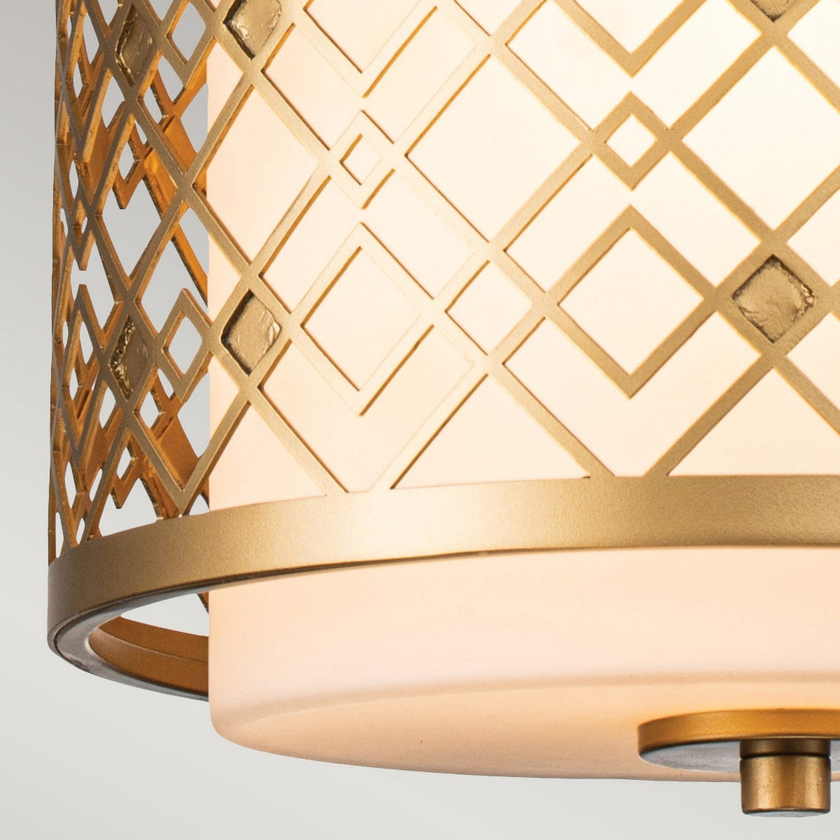 Close-up of the Ziggy 1 Light Duo-Mount Small Pendant/Semi-Flush in Lacquered Gold, showcasing its geometric, diamond-patterned metal frame with a lacquered gold finish encompassing a frosted white cylindrical shade that emits a soft warm glow. This versatile lighting solution adds elegance to any space.