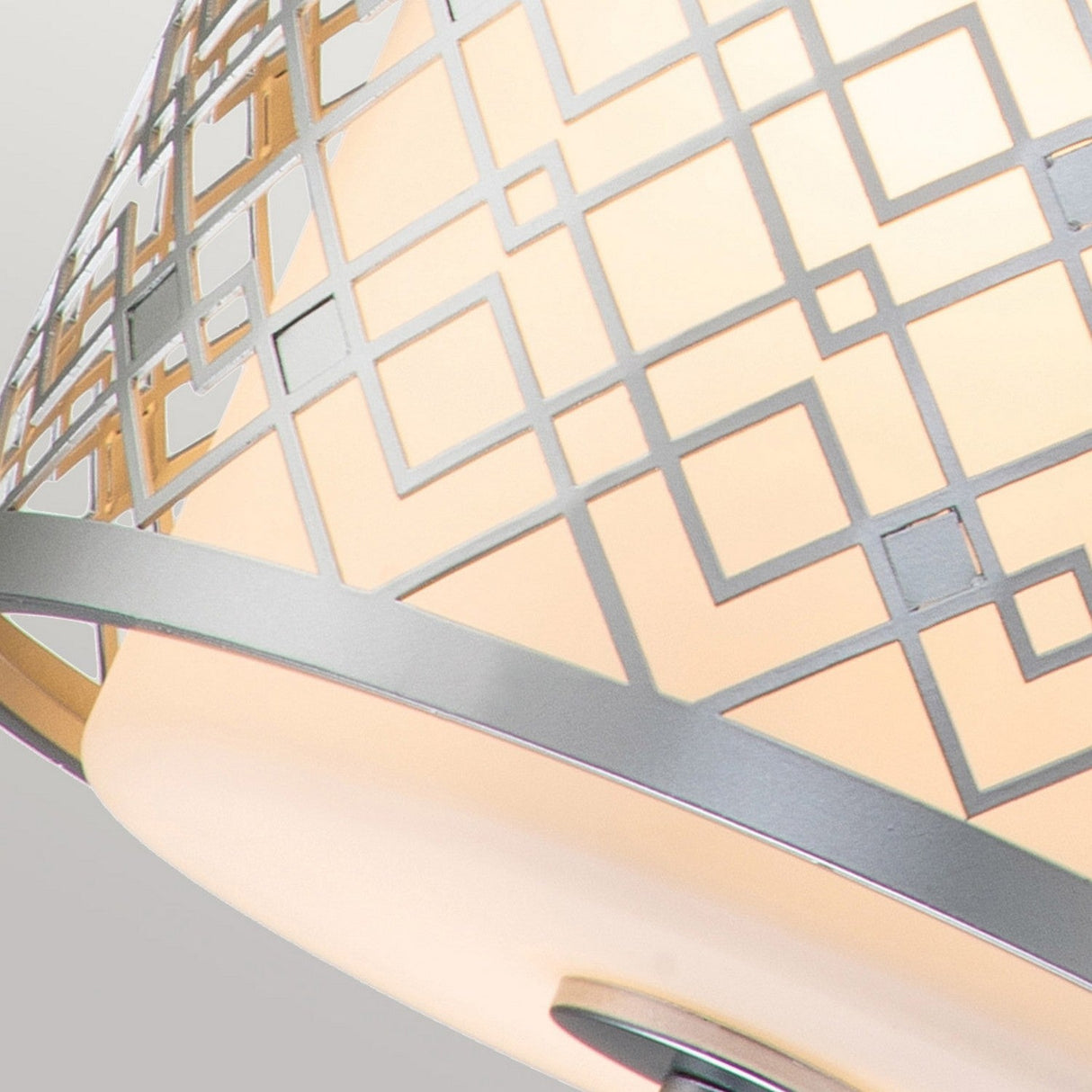 Close-up of a Ziggy 1 Light Duo-Mount Small Pendant/Semi-Flush - Lacquered Silver, featuring a geometric metal design. The pattern showcases intersecting squares that form a grid-like appearance. This modern lighting piece emits a soft, warm glow through frosted glass.
