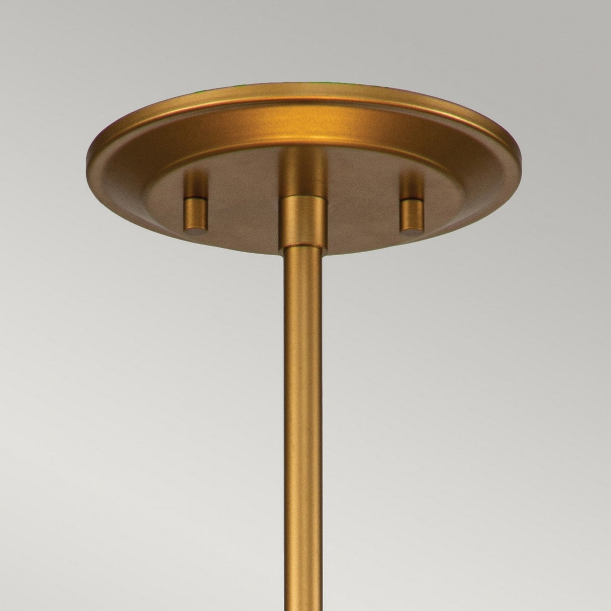 A close-up of the Ziggy 2 Light Duo-Mount Medium Pendant/Semi-Flush in lacquered gold highlights its contemporary design with a ceiling canopy and rod. The round plate at the top features a smooth, matte finish and an adjustable rod for customizable height. The background is plain and light gray.