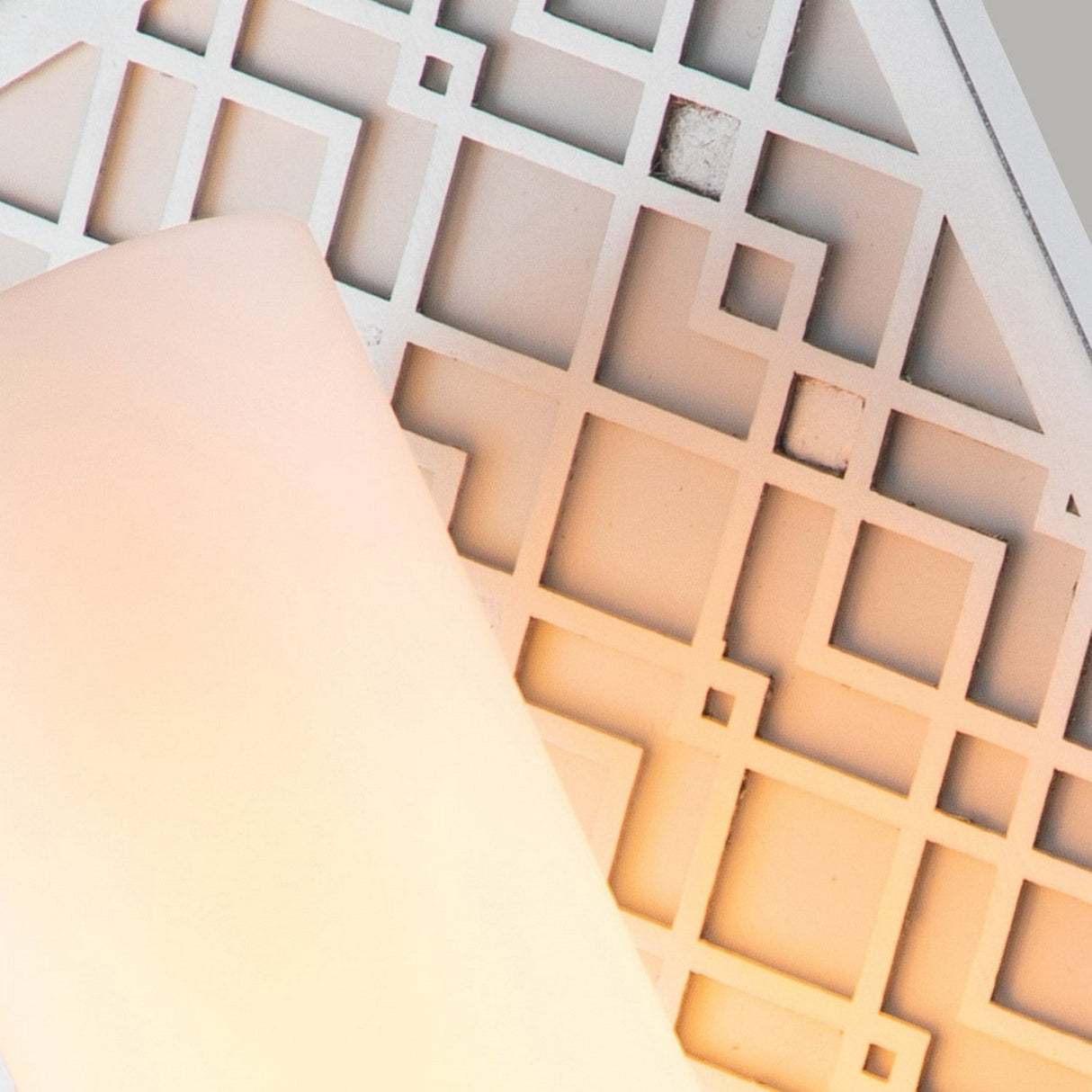 An up-close view of a surface adorned with a geometric pattern is softly illuminated by the Ziggy 1 Light Wall light - Lacquered Silver. The design showcases intersecting squares and rectangles with a lacquered silver finish, creating a contemporary and artistic aesthetic.