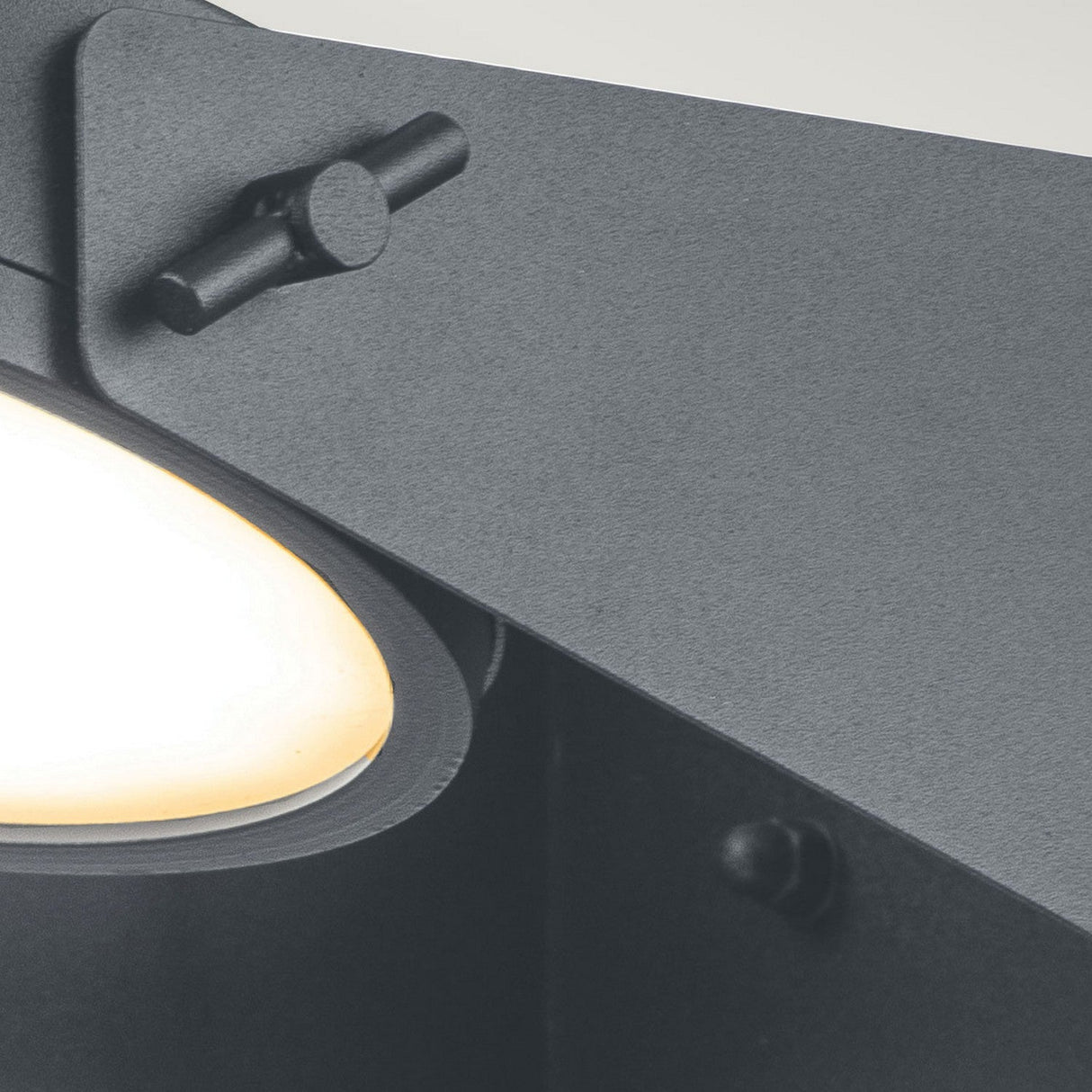 Close-up of the Zola Outdoor LED Wall Light in grey, showcasing its modern, minimalist design with an angled metal frame and a soft, warm light. Featuring visible screws and hinges, this industrial piece is crafted with weather-resistant stainless steel construction.