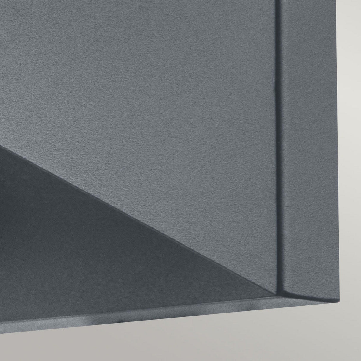 The image captures a close-up of a corner of the Zola Outdoor LED Wall Light - Grey, showcasing its sharp angles and straight edges. The matte grey finish, resembling stainless steel, contrasts beautifully with the lighter grey background to create a sleek and contemporary look.