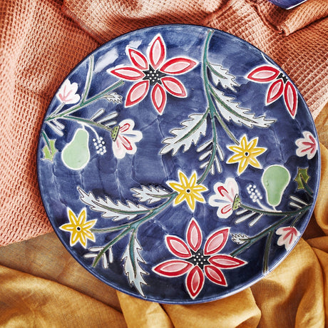 A navy stoneware side plate painted with red and yellow flowers on an orange cloth