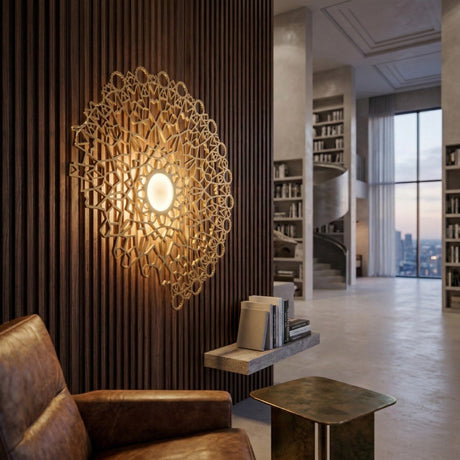 A modern living space featuring a Notredame LED Large Wall Light - Gold with intricate geometric design, a brown leather armchair, metallic side table, and a spiral staircase with built-in bookshelves.