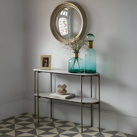 Narrow console table styled with vases, framed art, and décor below a round mirror, set against patterned flooring for an elegant entryway look.
