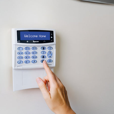 A home security system with a white and red alarm box, a remote control with four buttons, a white motion detector, and a small rectangular sensor.