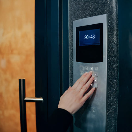 Home intercom system with a screen displayed. The screen shows a smiling woman. The device has buttons for navigation and phone functions.