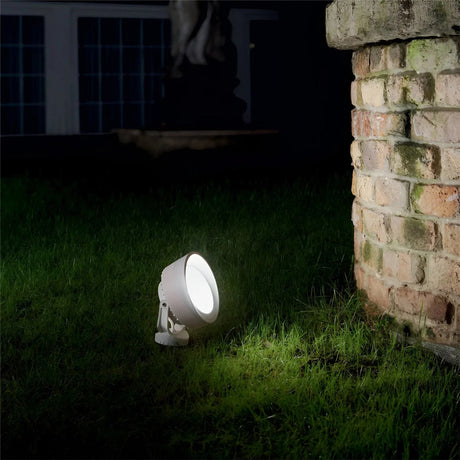 A spotlight illuminates a section of grass at night, placed near a brick structure, casting a bright light in the dark surroundings.