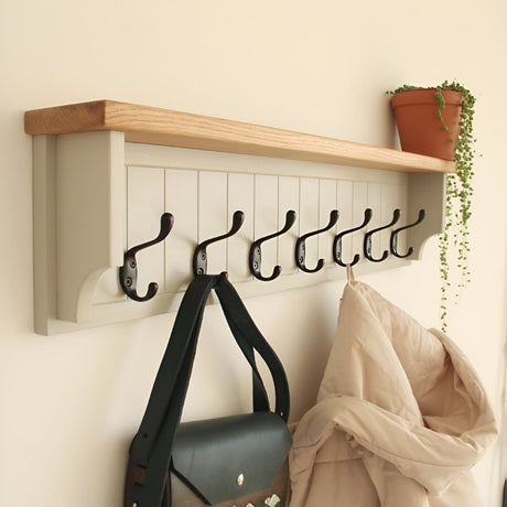 Wall-mounted coat rack with black hooks, a wooden top shelf, and hanging bags and textiles, styled with a small potted plant for an inviting entryway.