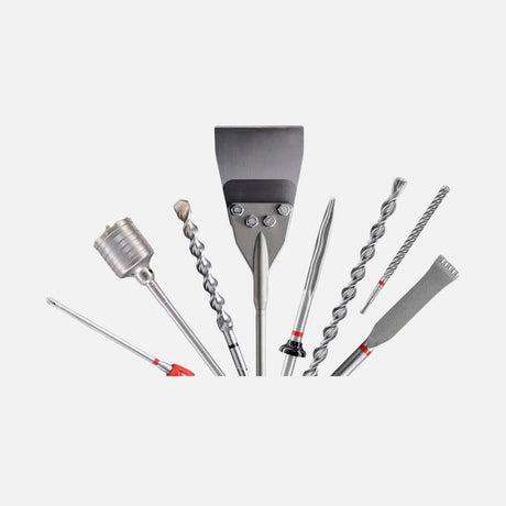 Set of assorted drill bits and chisels arranged in a row, including masonry bits, flat chisels, pointed bits, and a core drill head on a light background.