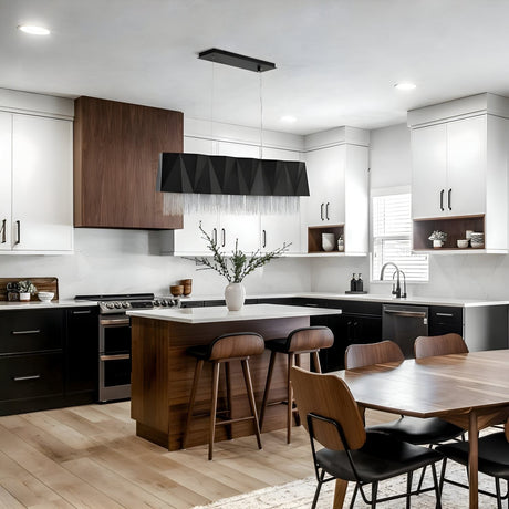 Modern kitchen with black and white cabinets, wood accents, a large island, sculptural black pendant light, and minimalist decor. A dining table with chairs is in the foreground. Fredrick Ramond logo below.