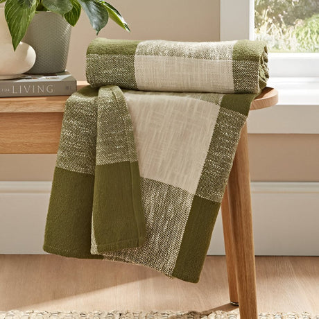 Folded green and cream throw blankets draped over a wooden stand in a bright room with natural decor touches.