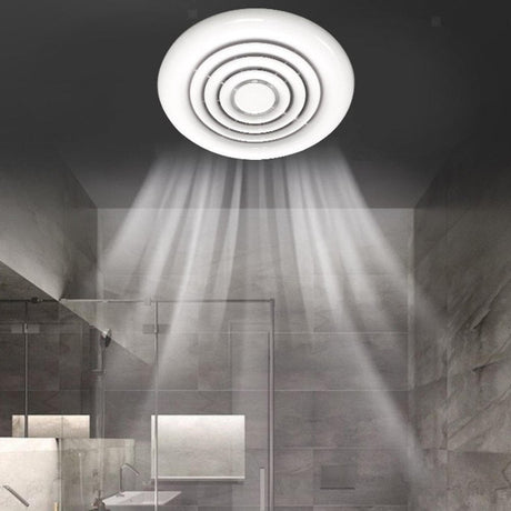 A white square ventilation fan with slatted grill cover is mounted on a wall. The design is sleek and modern, with a circular opening visible through the slats, designed for efficient airflow.