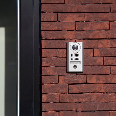 Wall-mounted white intercom phone with coiled cord, next to a black and gray doorbell panel featuring a central button.