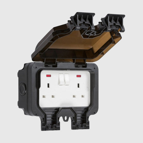 A black weatherproof outdoor electrical outlet with a hinged cover open, revealing two UK-style sockets. The cover has two locks on top, showcasing protection against the elements.