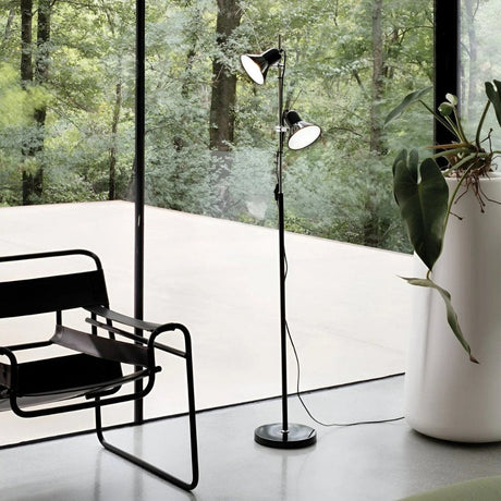 Modern black floor lamp beside a chair with large windows overlooking greenery.
