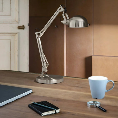 Adjustable metal desk lamp on wooden table with cup and notebooks.