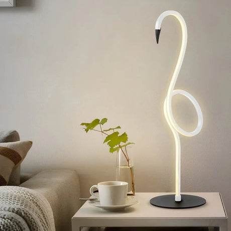 Flamingo-shaped neon table lamp glowing softly beside a plant and mug.