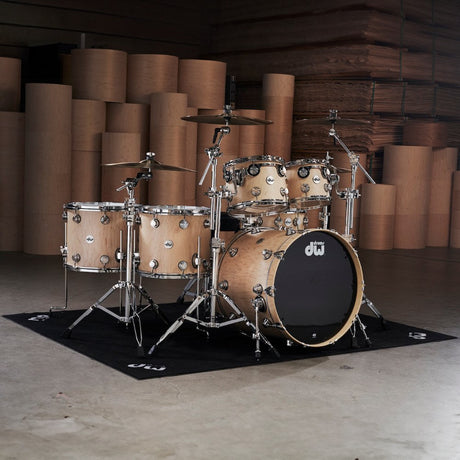 Full acoustic drum kit in natural wood finish set up in a studio with stacked wooden panels in the background.