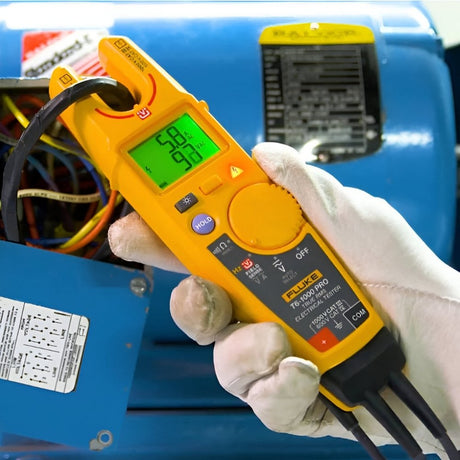 Electrician using a handheld voltage tester near industrial equipment.