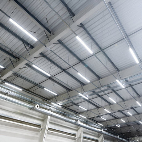 Industrial ceiling with bright linear LED lights in a large warehouse space.