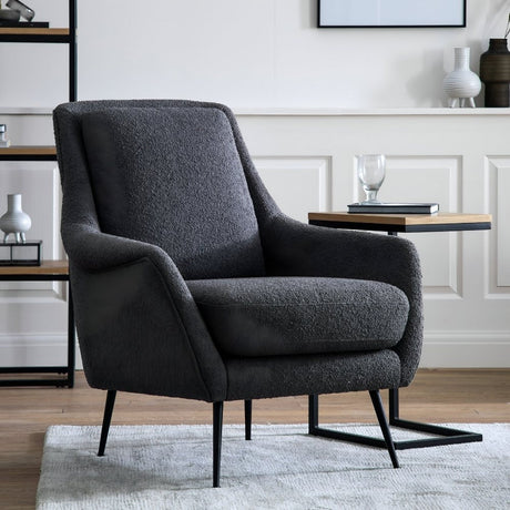Dark grey modern armchair featuring clean lines and slim metal legs, set in a bright living room with soft decor, a side table, and minimalist artwork on the surrounding walls.