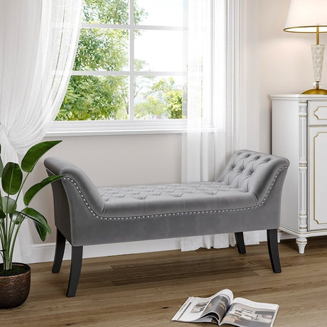 Grey upholstered chaise bench with button-tufted detailing, placed in a softly lit room near a large window, styled with minimal accessories for a calm, refined atmosphere.