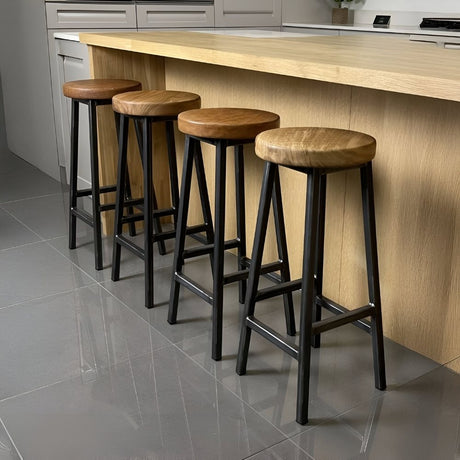 Set of wooden bar stools with round seats and black metal legs, lined along a modern kitchen island with clean surfaces, creating a warm mix of industrial and natural style.