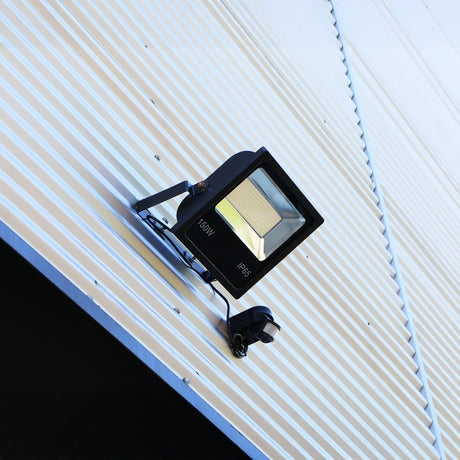 Mounted LED floodlight fixed to a ribbed metal exterior wall, designed for outdoor illumination and security lighting.