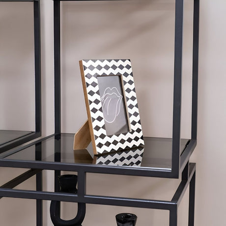 Chevron-patterned photo frame displayed on a black metal shelf with glass surfaces, styled against a neutral wall to create a clean, modern decorative accent within the room.