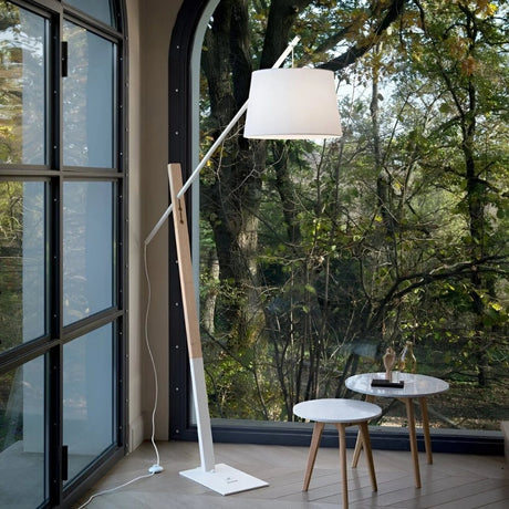 Floor lamp beside windowed wall with outdoor forest view and small table.