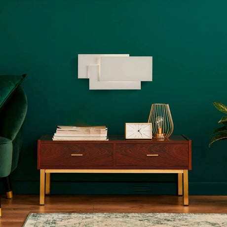 Mid-century console against dark green wall with decor and table lamp.