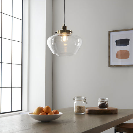 Kedleston Pendant in brass with a clear rounded glass shade, hanging above a wooden dining table in a kitchen setting.