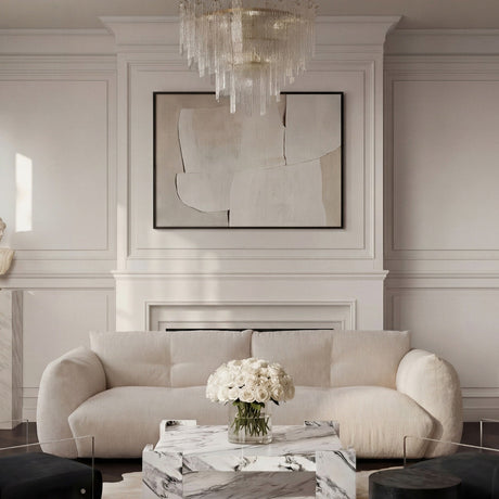 A curved pearl chenille three-seater sofa beside a marble coffee table and white roses, under a glass chandelier