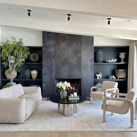 A living room with a cream sofa, two armchairs and a round black and chrome coffee table in front of a dark fireplace wall